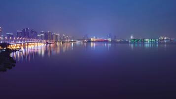 A nighttime cityscape with a waterfront, illuminated buildings, and a bridge reflecting on the water.