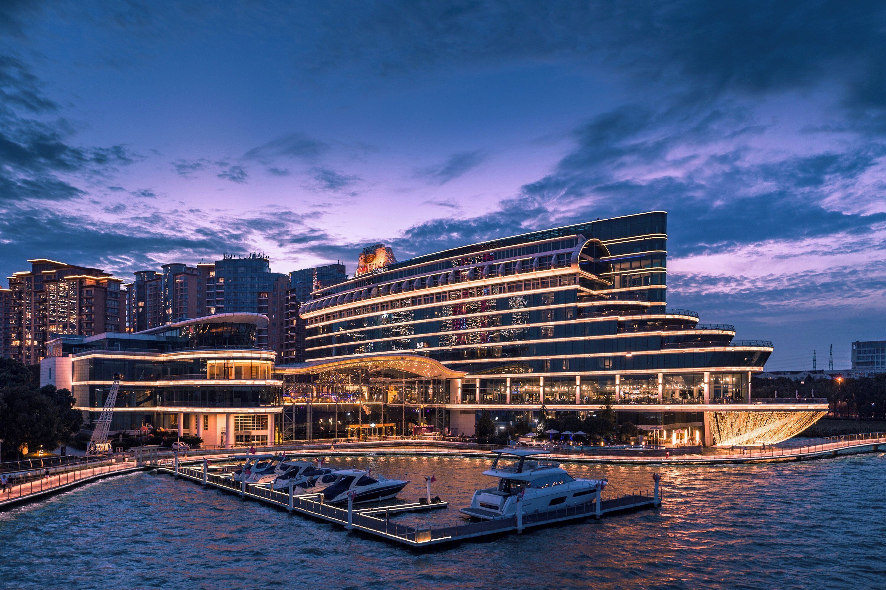 A waterfront hotel with a modern design, featuring multiple balconies and a marina with boats.