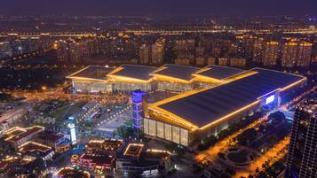 A large, multi-story building with a flat roof, surrounded by a well-lit urban area at night.