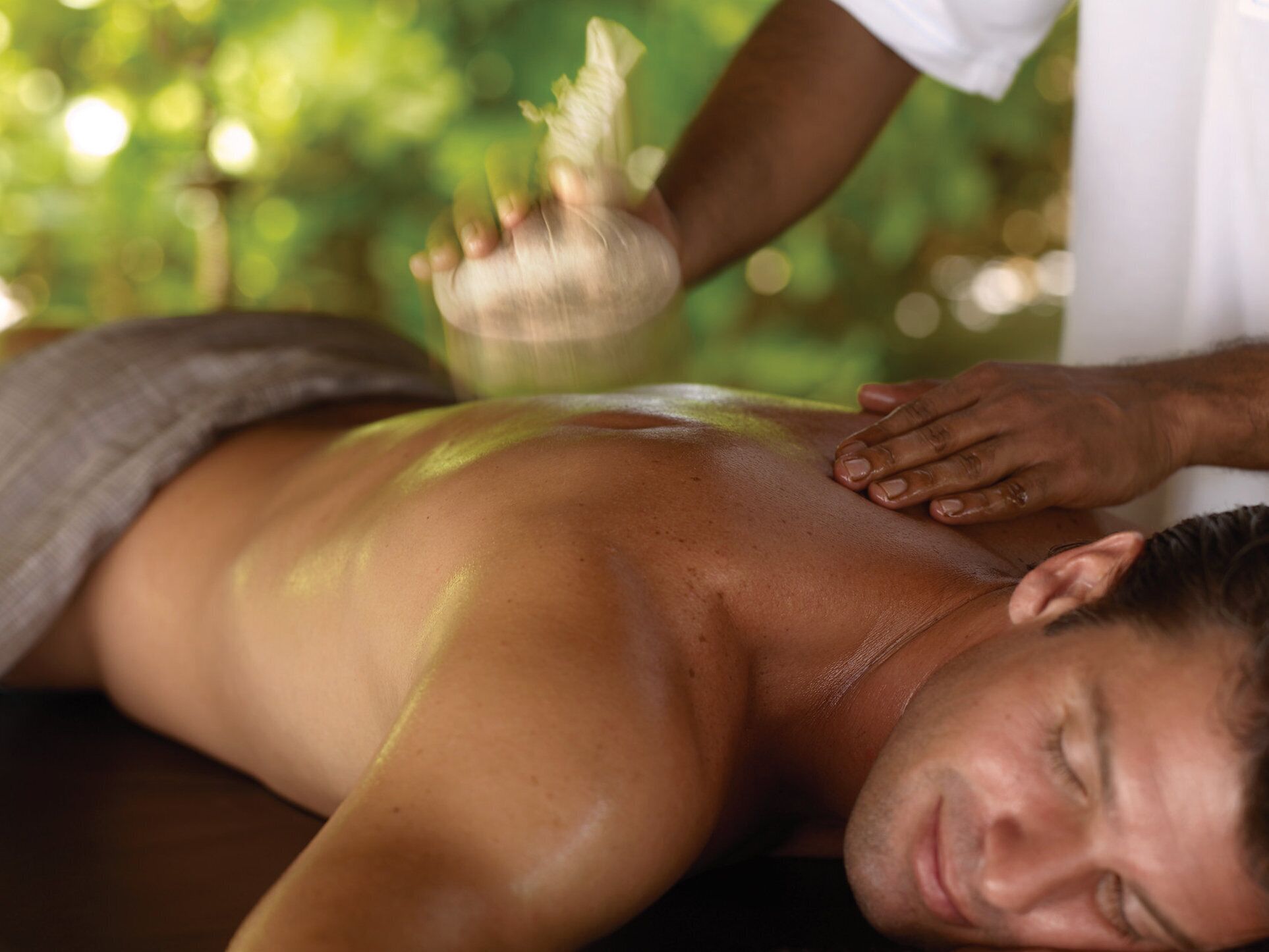 A person receiving a back massage with a towel draped over their lower body.
