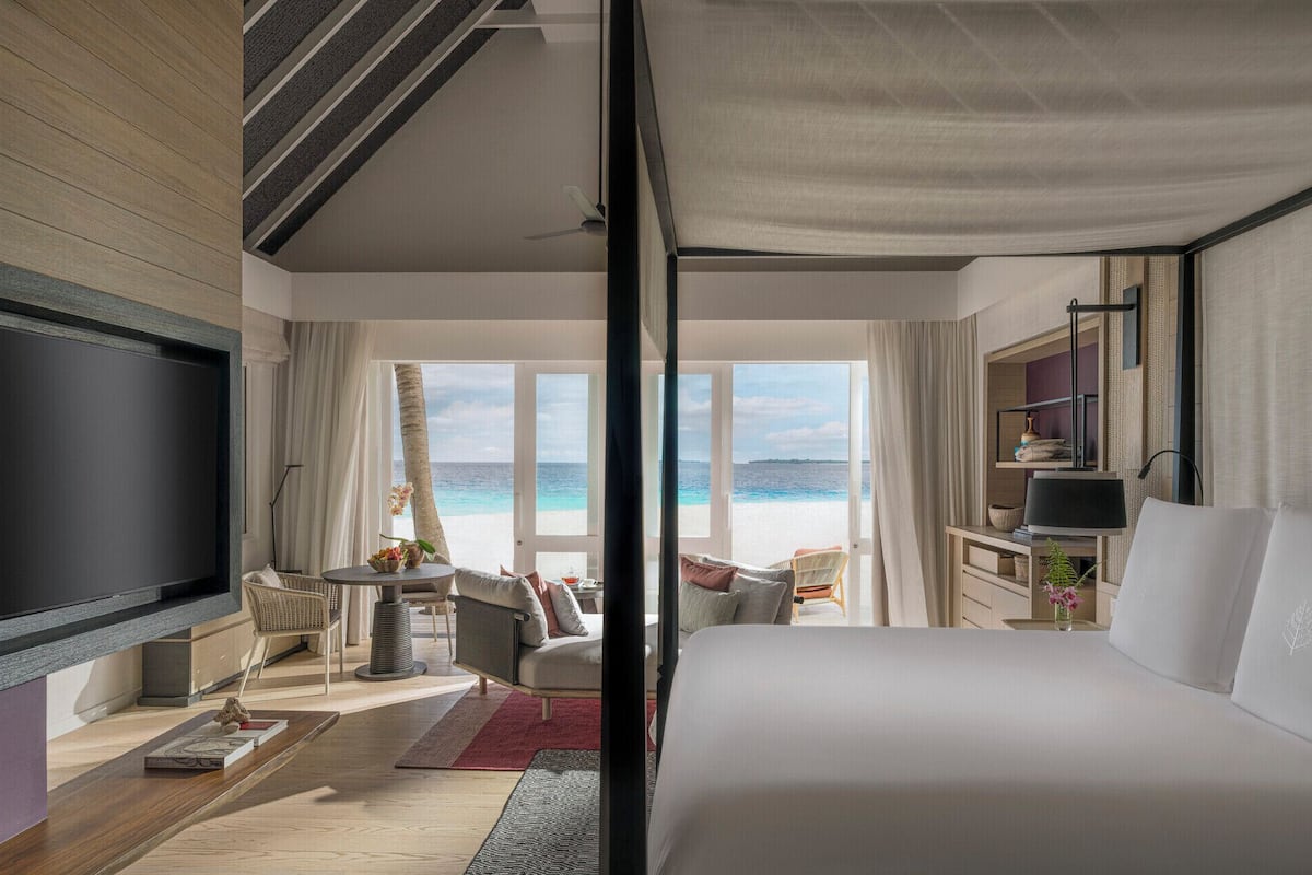Ein Hotelzimmer mit Bett, Sitzecke, Fernseher und Blick auf den Strand.