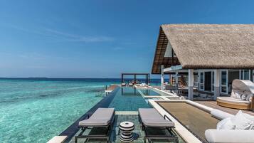 Une piscine à débordement avec des chaises longues et une structure au toit de chaume offrant une vue sur l’océan.