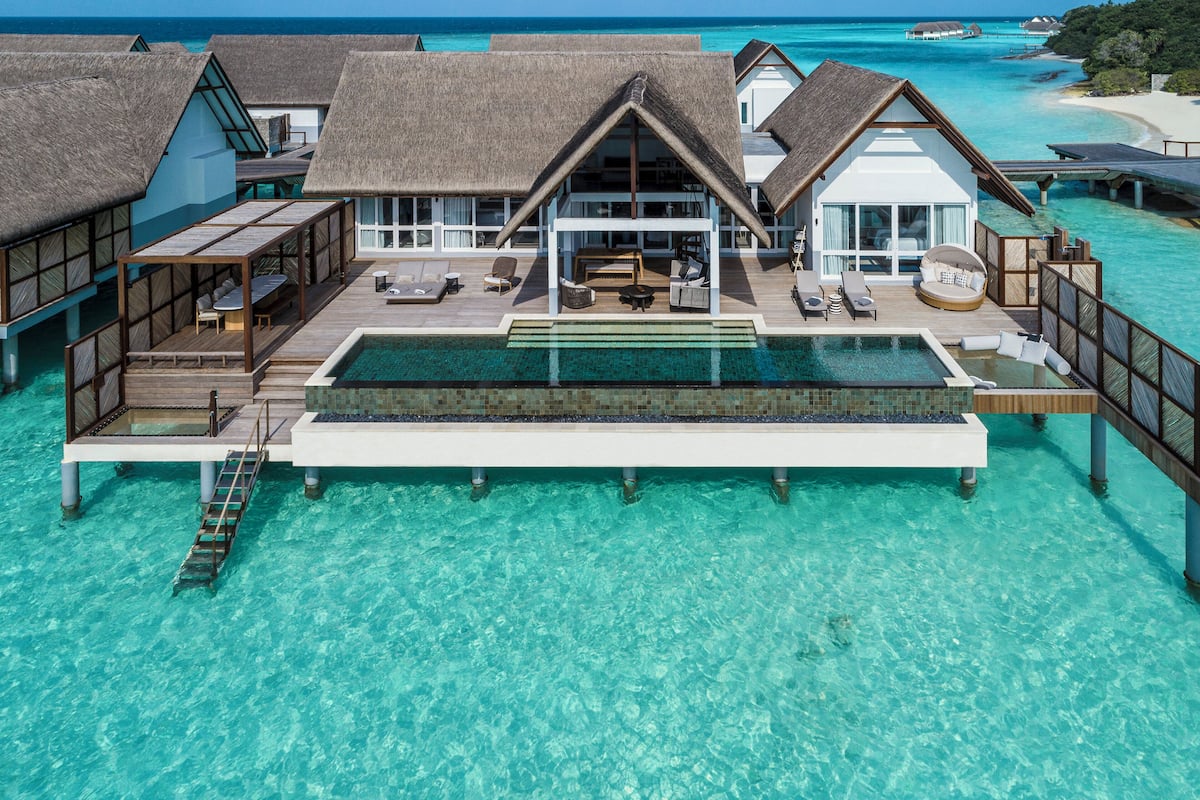 Eine Wasserbungalow mit Swimmingpool, Loungebereichen und Blick auf das türkisfarbene Meer.