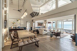 A spacious living area with a large dining table, comfortable seating, and a view of the ocean.