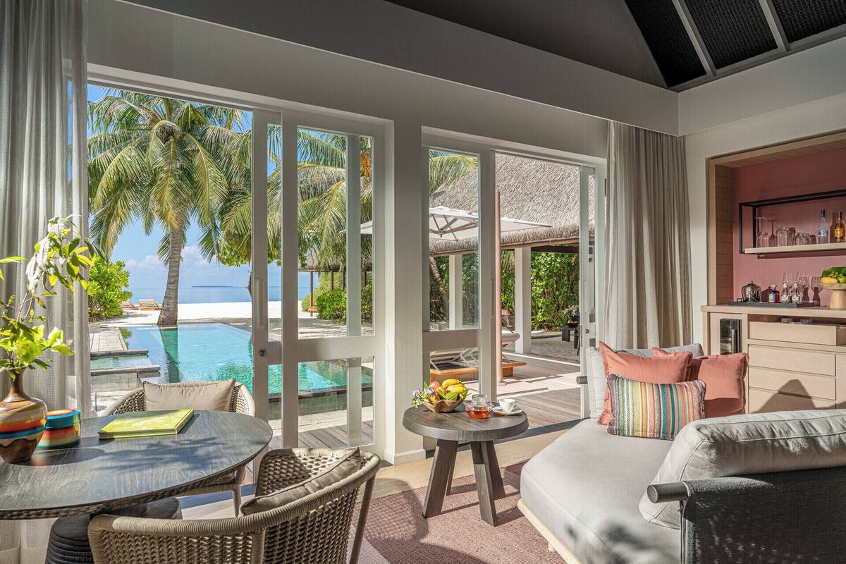 Ein großzügiger Wohnbereich mit Blick auf einen Pool und Palmen, ausgestattet mit einer Couch, Sesseln und einem kleinen Tisch.