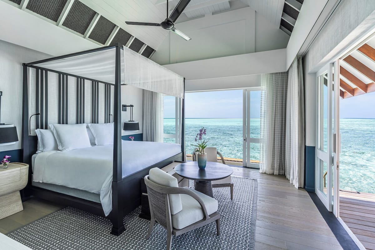 Ein Himmelbett mit Blick auf das Meer, ein kleiner Tisch mit einer Vase und ein Sessel.