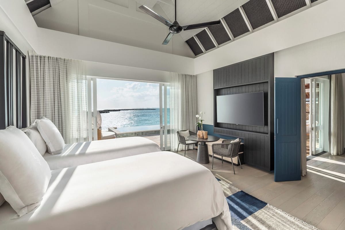 Ein modernes Hotelzimmer mit zwei Betten, einem Fernseher, einem Balkon mit Meerblick und einem Deckenventilator.