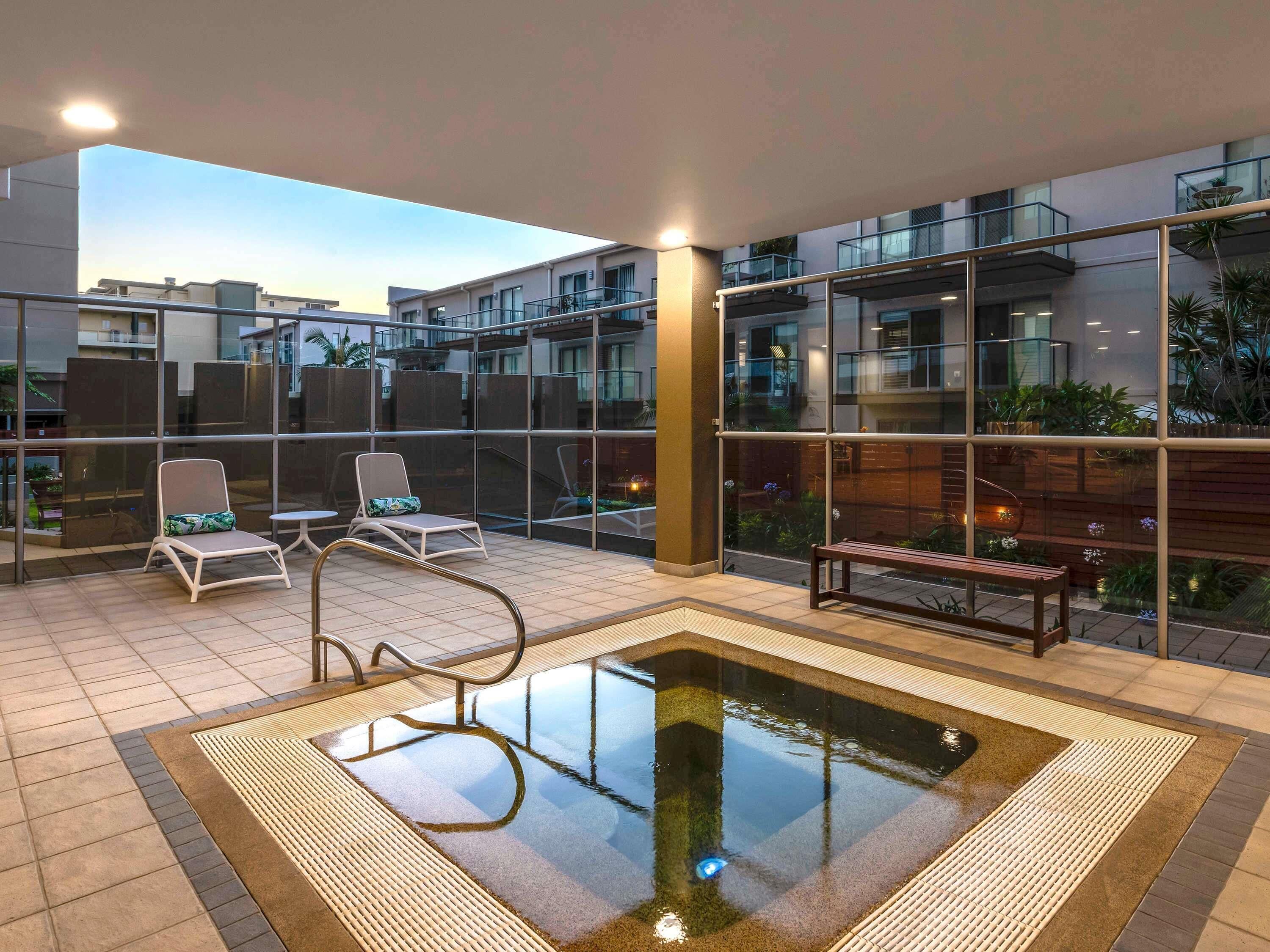 Un área de piscina en la azotea con sillones de descanso, una piscina pequeña y vistas de edificios circundantes.
