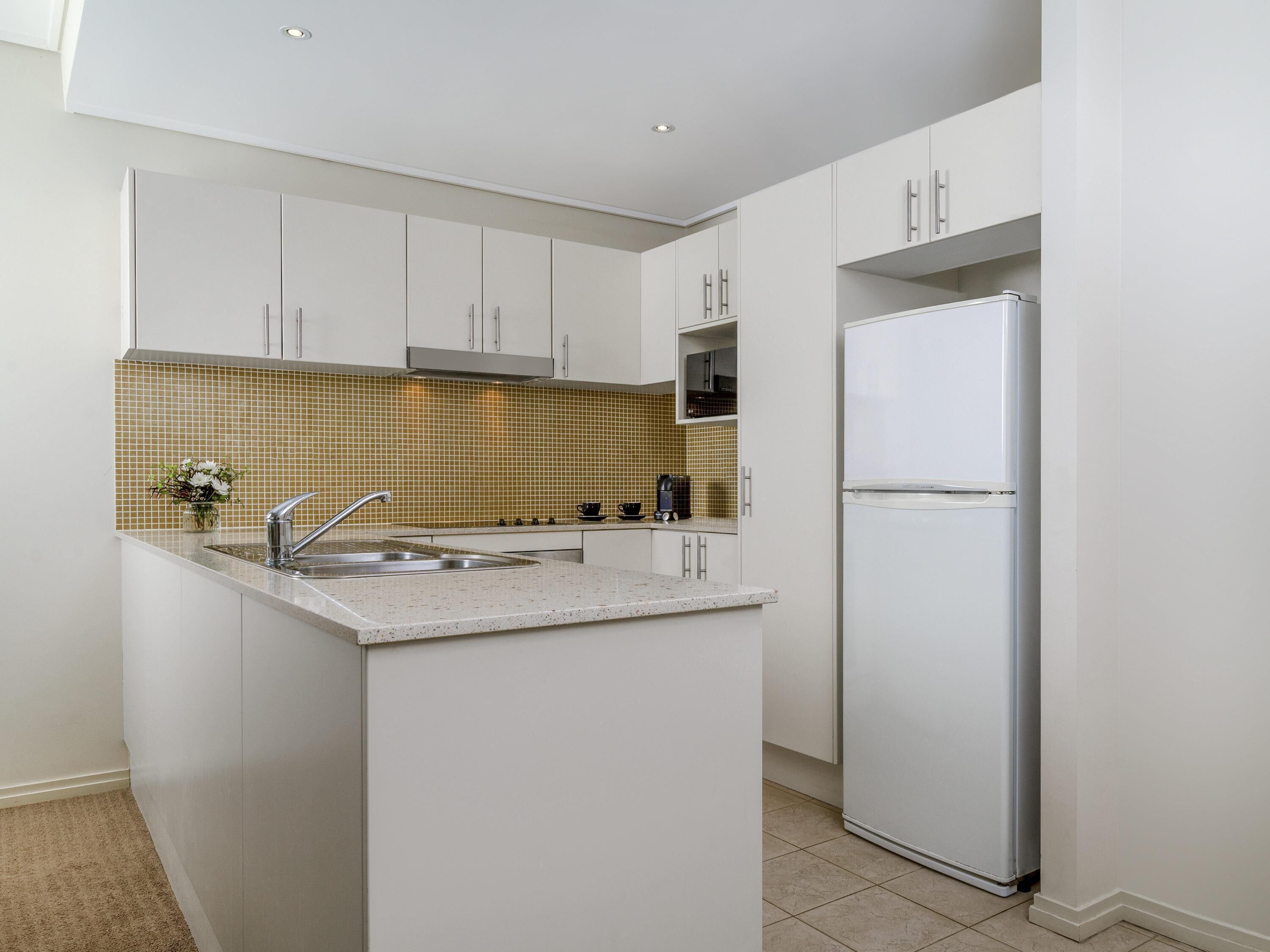 A modern kitchen with white cabinets, a stainless steel sink, and a built-in oven.