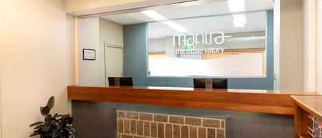 A reception desk with a mirror reflecting the interior, a potted plant, and a framed certificate on the wall.