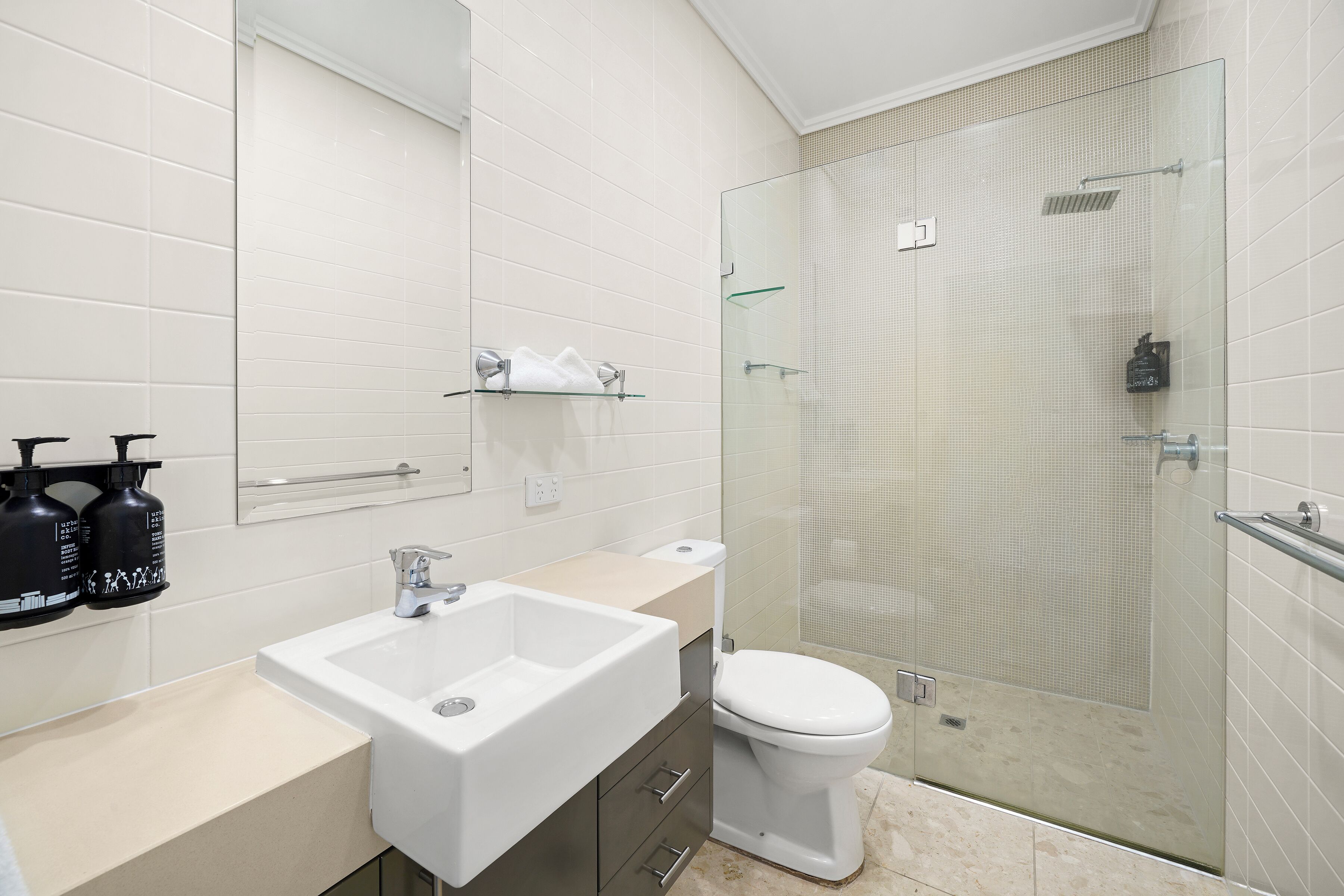 Et moderne badeværelse med hvid vask, toilet og brusekabine med glas.