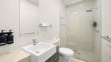 Et moderne badeværelse med hvid vask, toilet og brusekabine med glas.