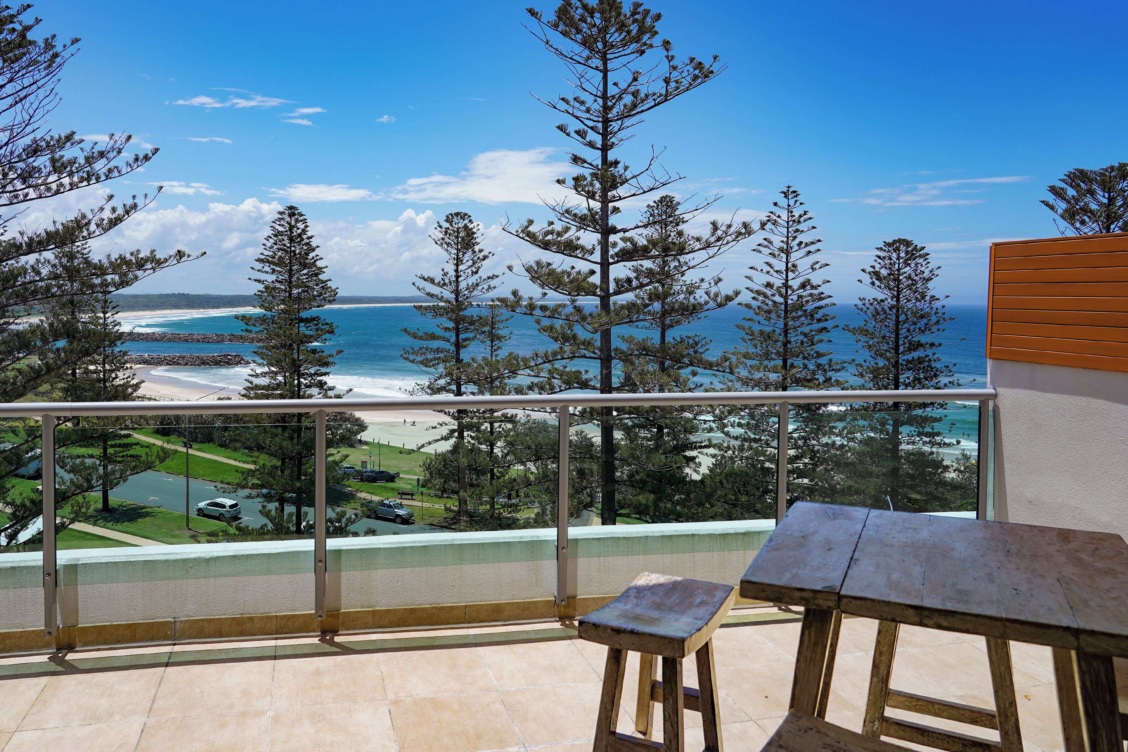 A balcony with a view of the ocean and beach, a wooden table, and a railing.
