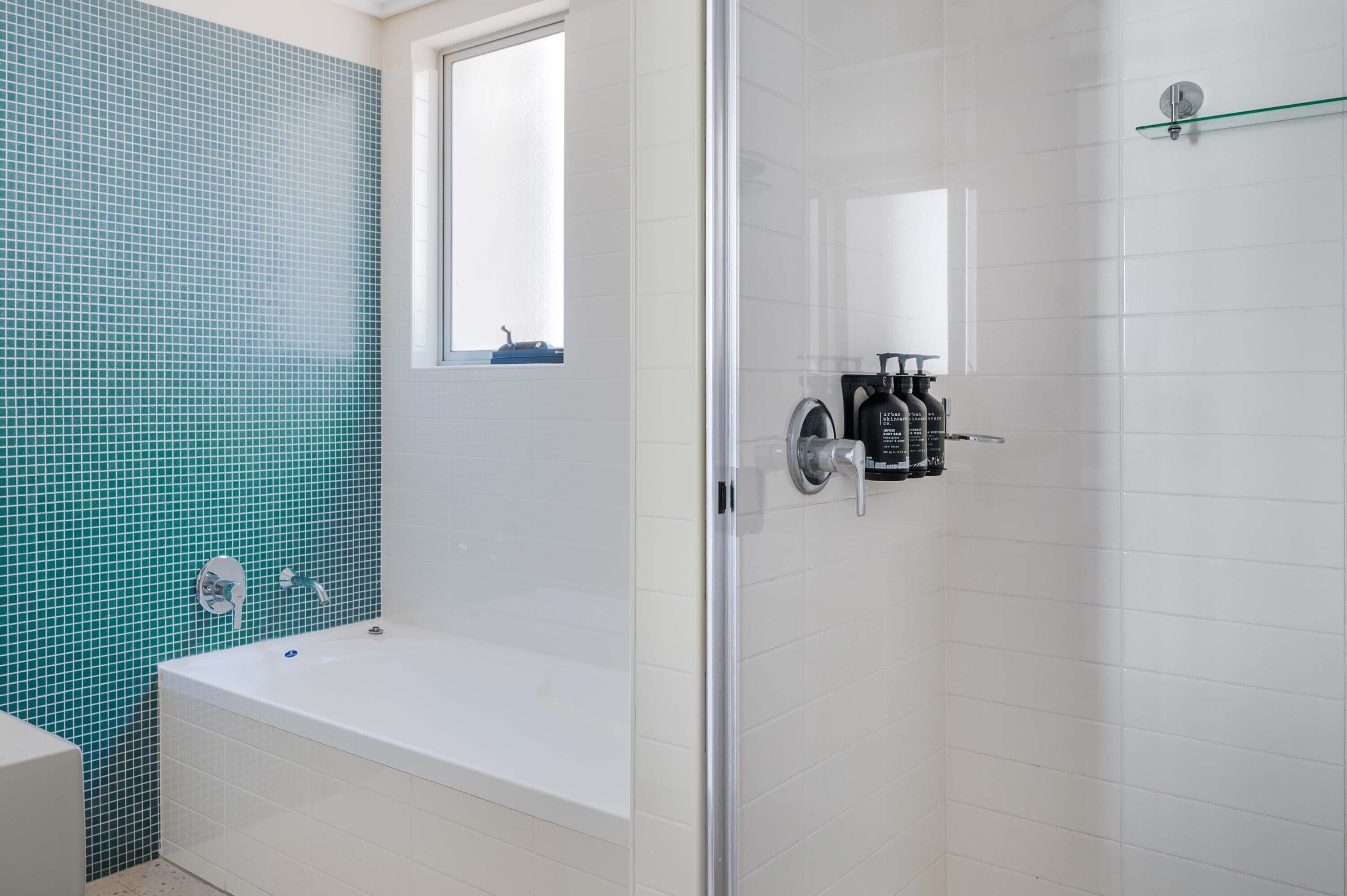 A modern bathroom with a bathtub, a glass shower enclosure, and a window.