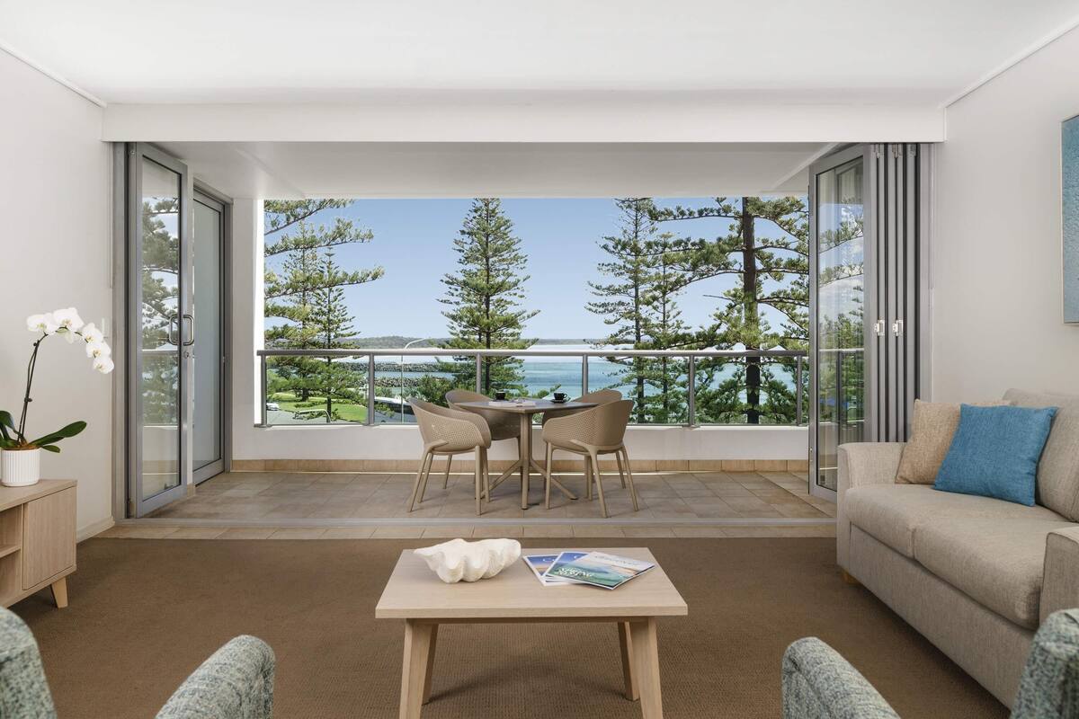 A modern living room with a balcony, a sofa, a coffee table, and a view of the sea.