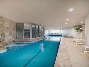 Una piscina interior con agua cristalina, una pared de piedra y una zona de estar con sillas blancas.