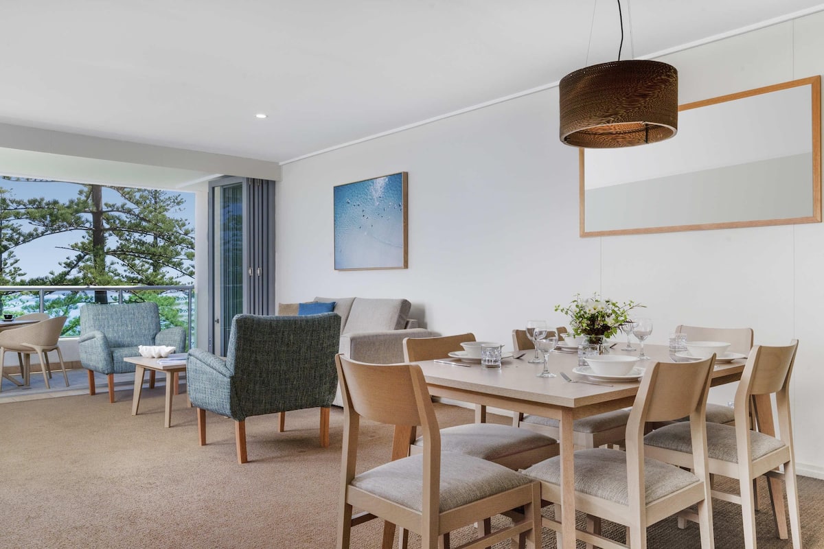 A modern dining area with a wooden table, chairs, and a hanging light fixture.
