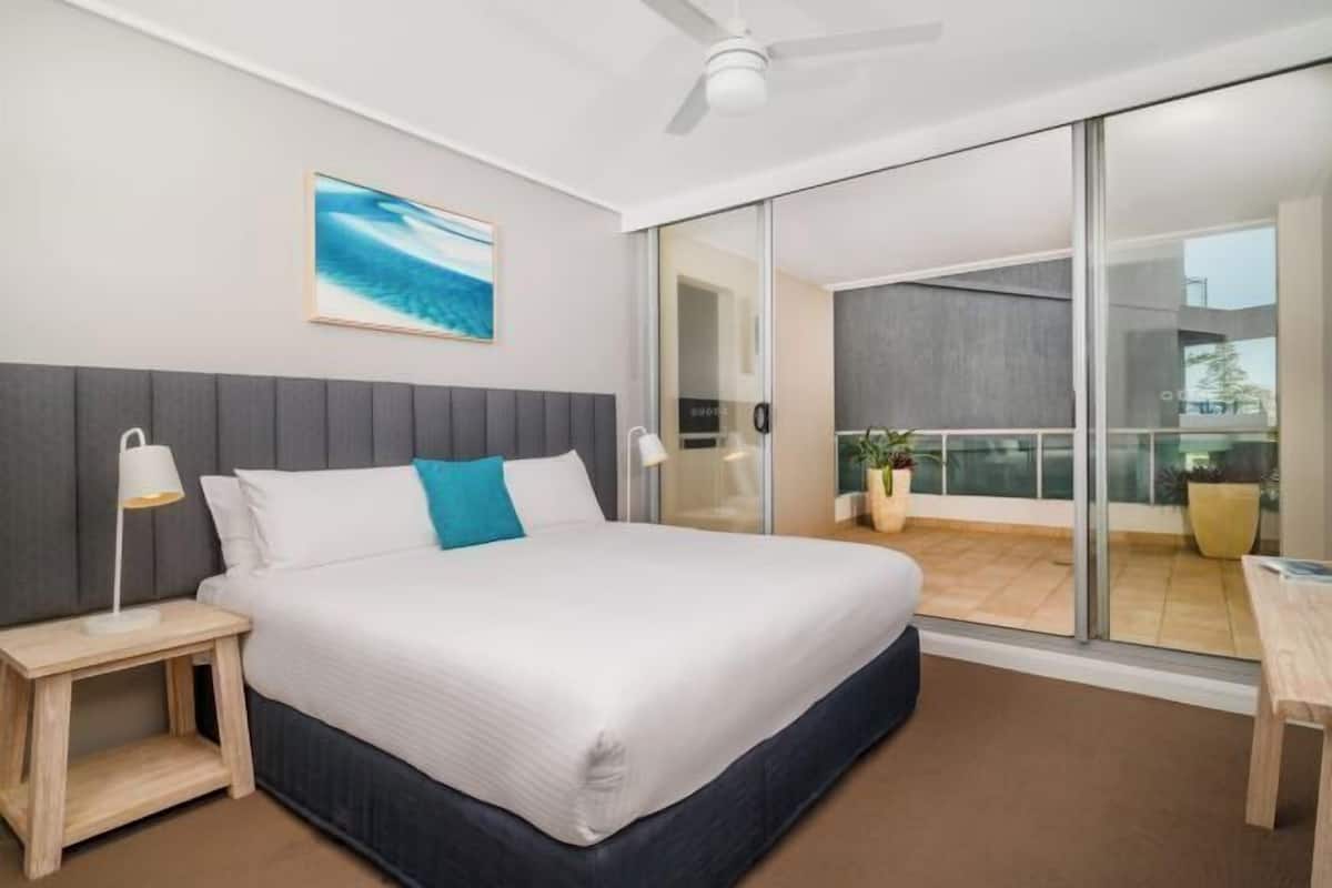 A modern hotel room with a bed, bedside lamps, a painting, and a balcony with a view.