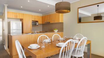 Una cocina moderna con armarios de madera, microondas integrado y comedor con mesa de madera y sillas blancas.