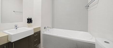 A modern bathroom with a white sink, dark cabinets, a large bathtub, and a shower area.