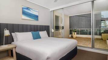 A modern hotel room with a large bed, a ceiling fan, a view through a sliding glass door, and a painting on the wall.