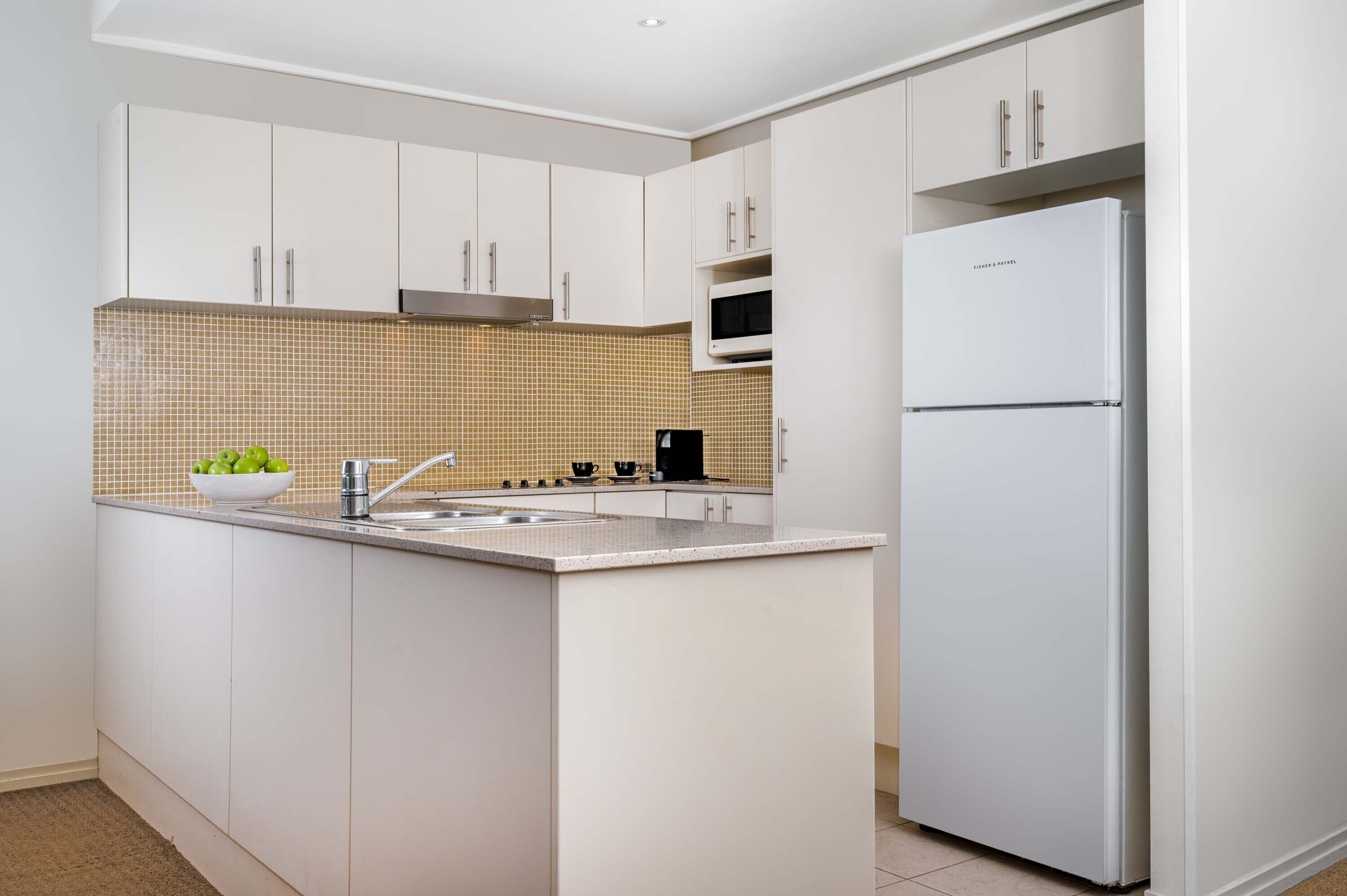 A modern kitchen with white cabinetry, a built-in microwave, and a stainless steel refrigerator.