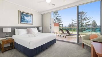 A hotel room with a bed, a nightstand, a desk, a chair, a balcony with a view, and a ceiling fan.