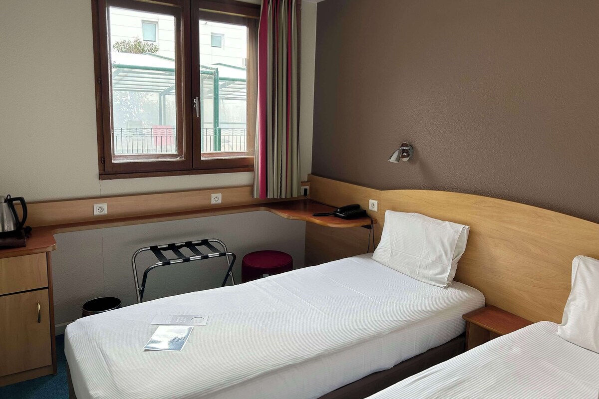 Habitación de hotel con cama, escritorio, silla, mesita y ventana con cortinas.