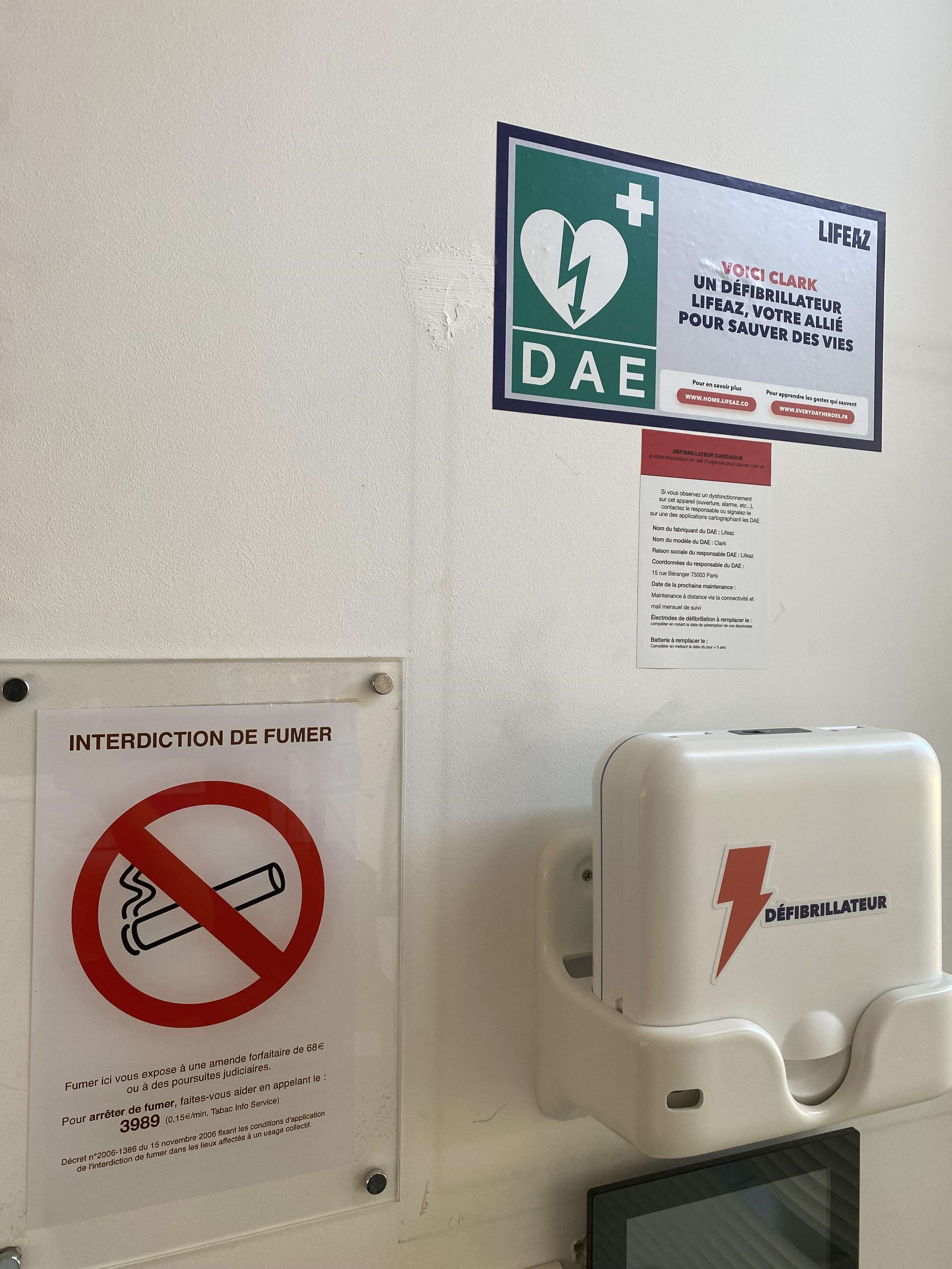 Eine Wand mit einem DAE-Defibrillator, einem Rauchverbotsschild und einem LifeZ-Pulsoximeter.
