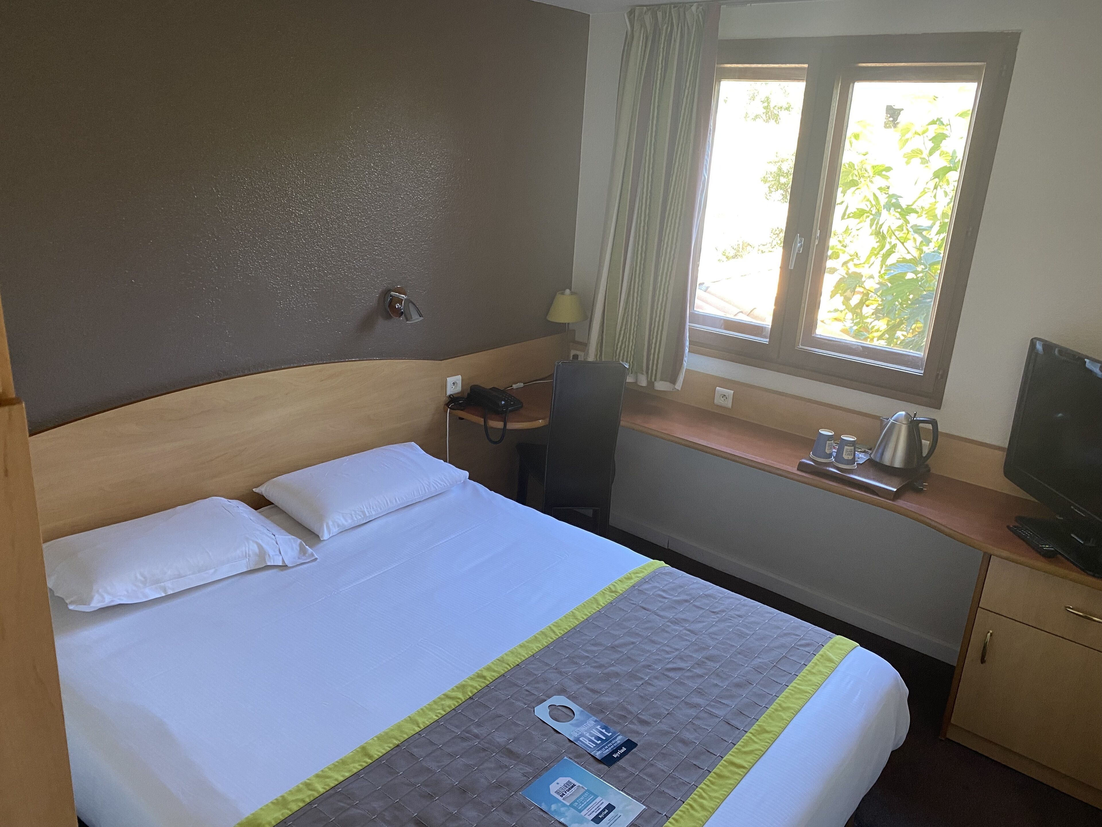 A hotel room with a bed, a desk with a computer, a television, and a window with curtains.