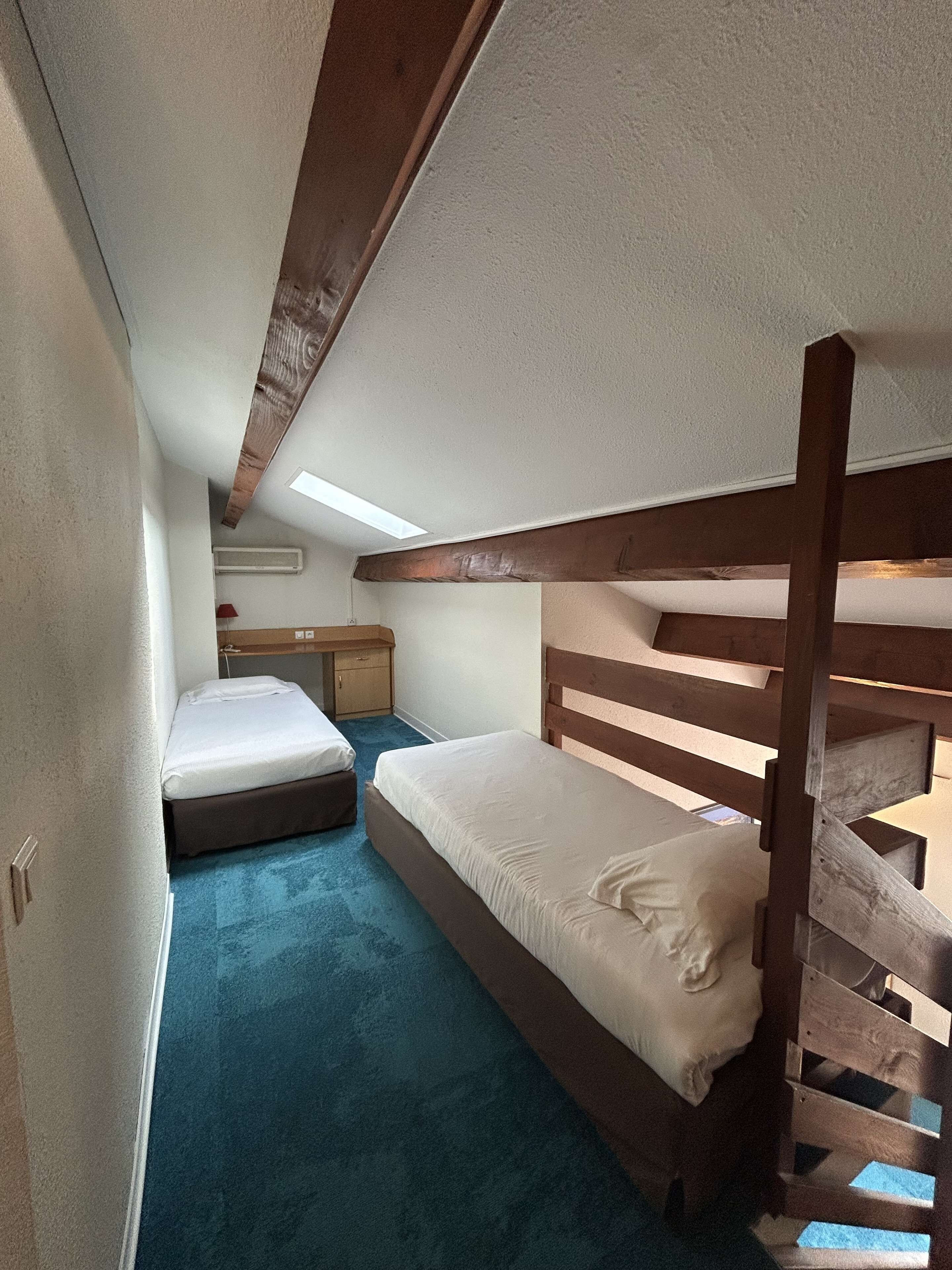 Eine kleine, einsprachige Holzhütte mit Etagenbetten, einem Schreibtisch und einem kleinen Fenster.