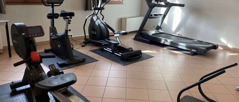 Une salle de sport à domicile équipée d’un vélo d’appartement, d’un appareil elliptique, d’un tapis de course et de poids.