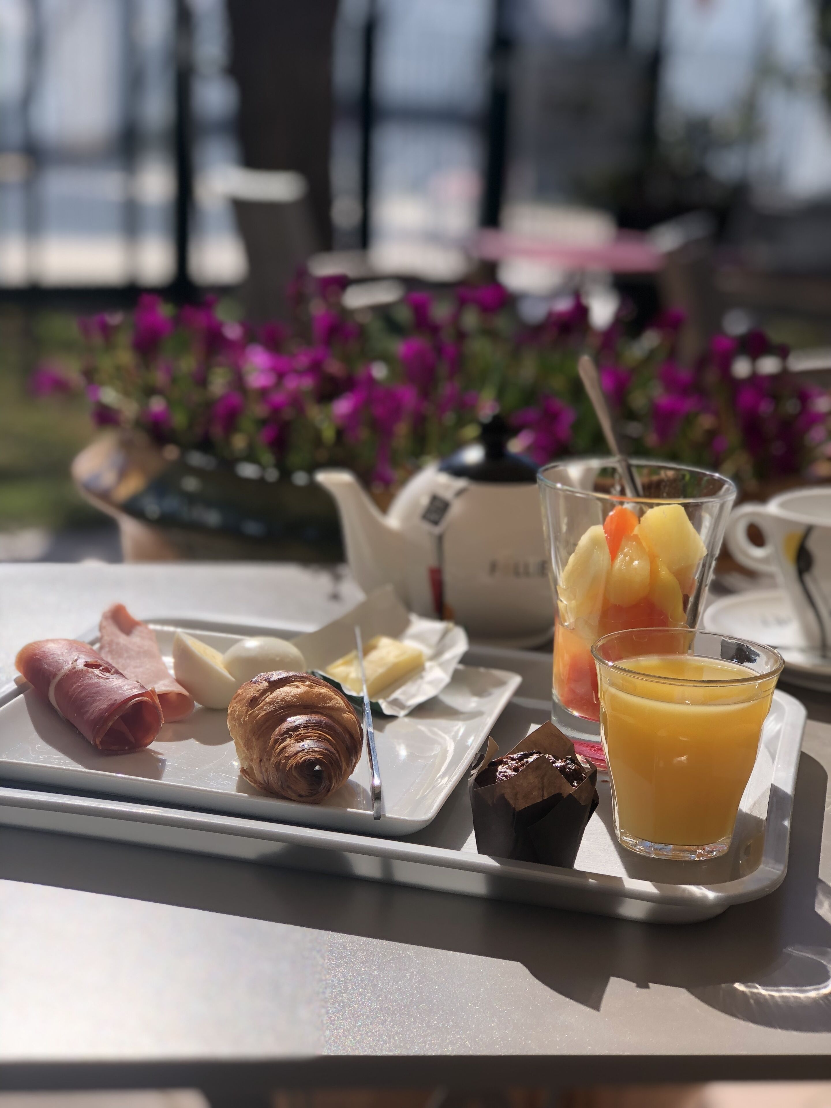 A breakfast tray with croissants, ham, eggs, butter, fruit, and orange juice.