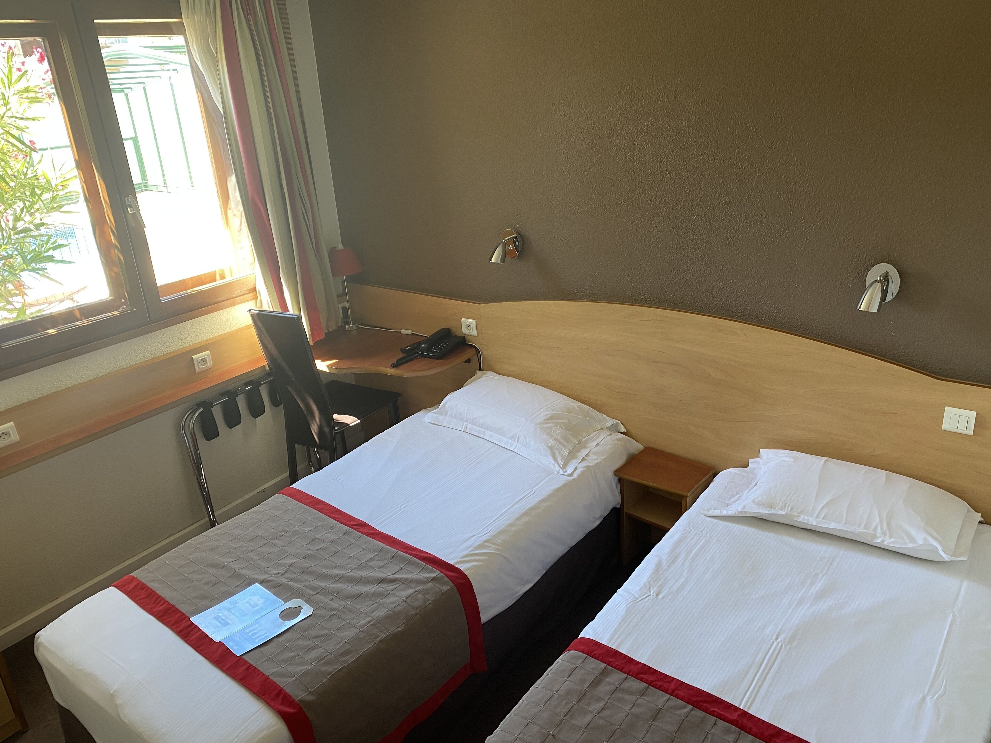 A hotel room with two beds, a desk, a chair, and a window with curtains.