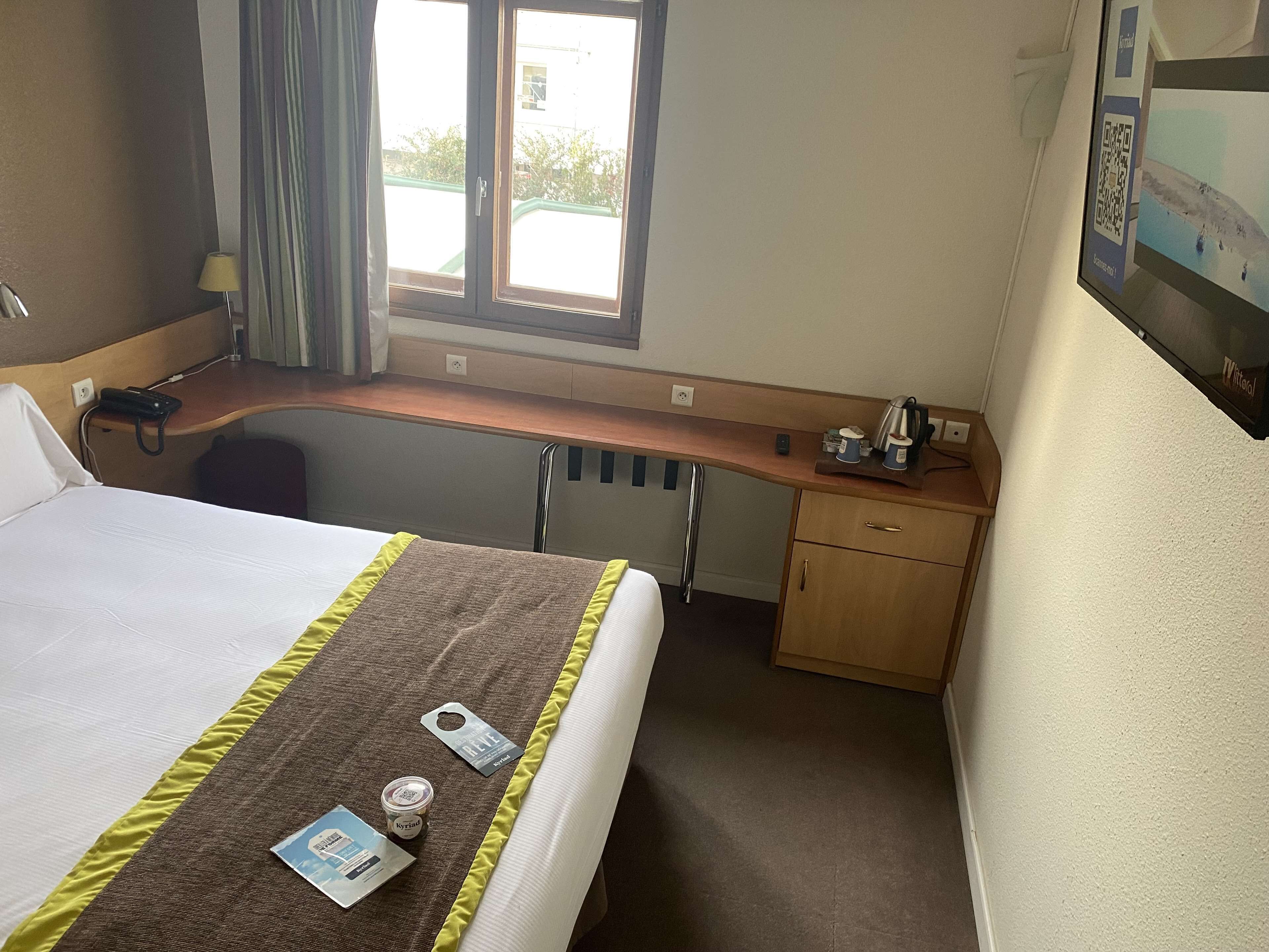 Een hotelkamer met een bed, een bureau, een stoel, een raam en een televisie aan de muur.