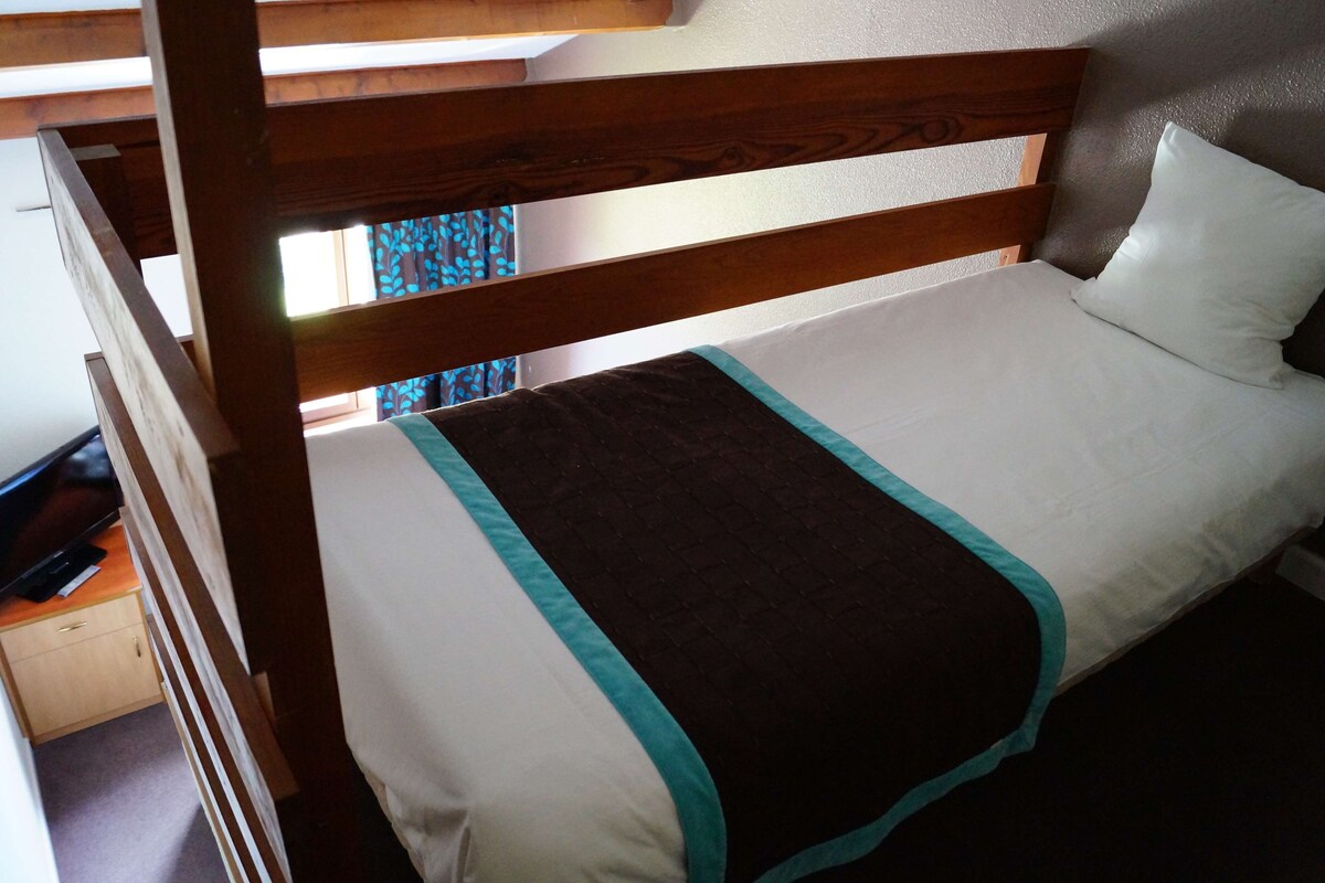 Una cama litera con estructura de madera, ropa de cama blanca y un detalle en color turquesa.