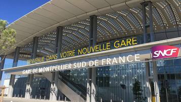 Um edifício moderno com uma placa que diz “BIENVENUE DANS VOTRE NOUVELLE GARE” e “GARE DE MONTPELLIER SUD DE FRANCE”.