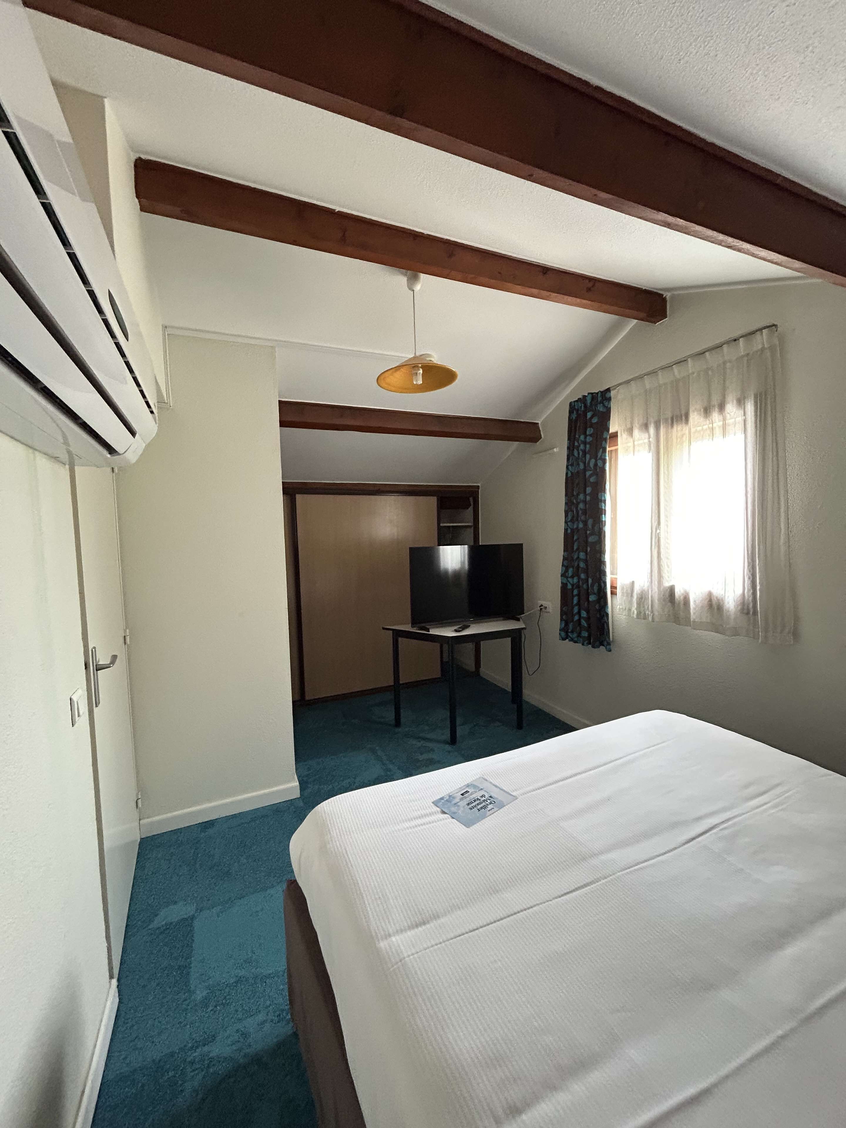 Una camera d'albergo con un letto, una TV, una scrivania e un condizionatore d'aria.