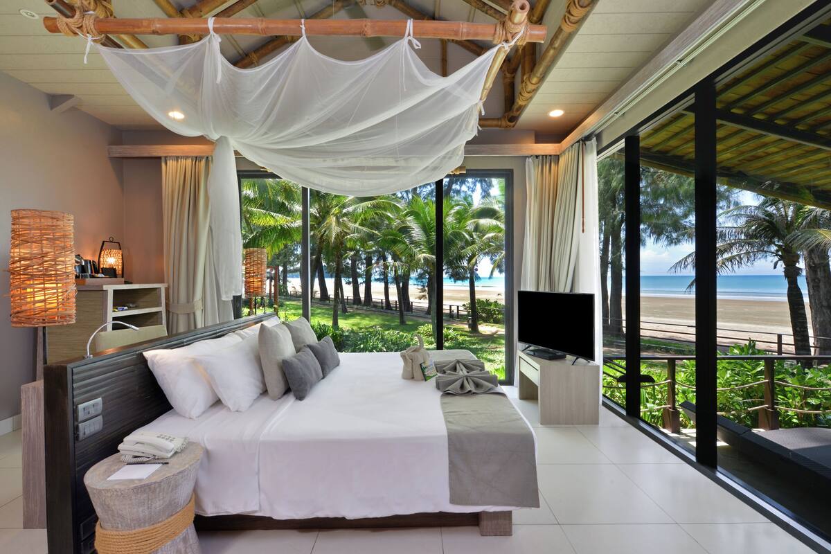 A spacious bedroom with a large bed, a TV, and a view of the beach.