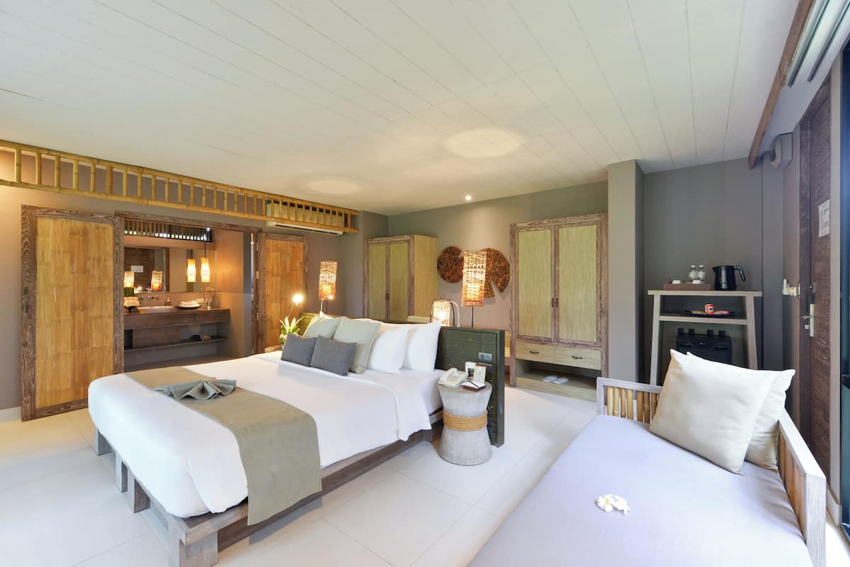 A modern hotel room with a large bed, a smaller bed, a vanity with a mirror, and a small table with a lamp.