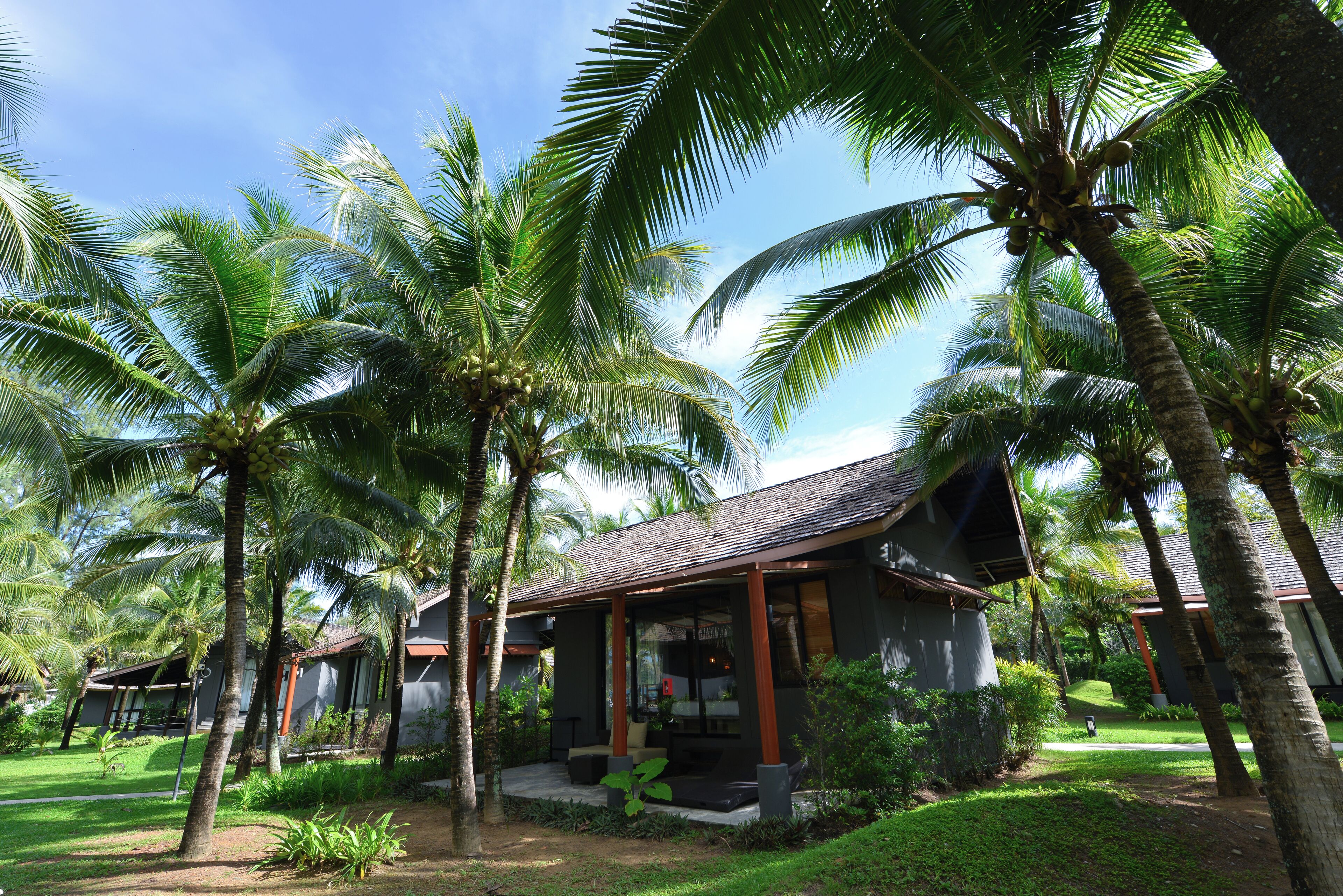 A resort with multiple palm trees, a covered outdoor seating area, and a building with a tiled roof.