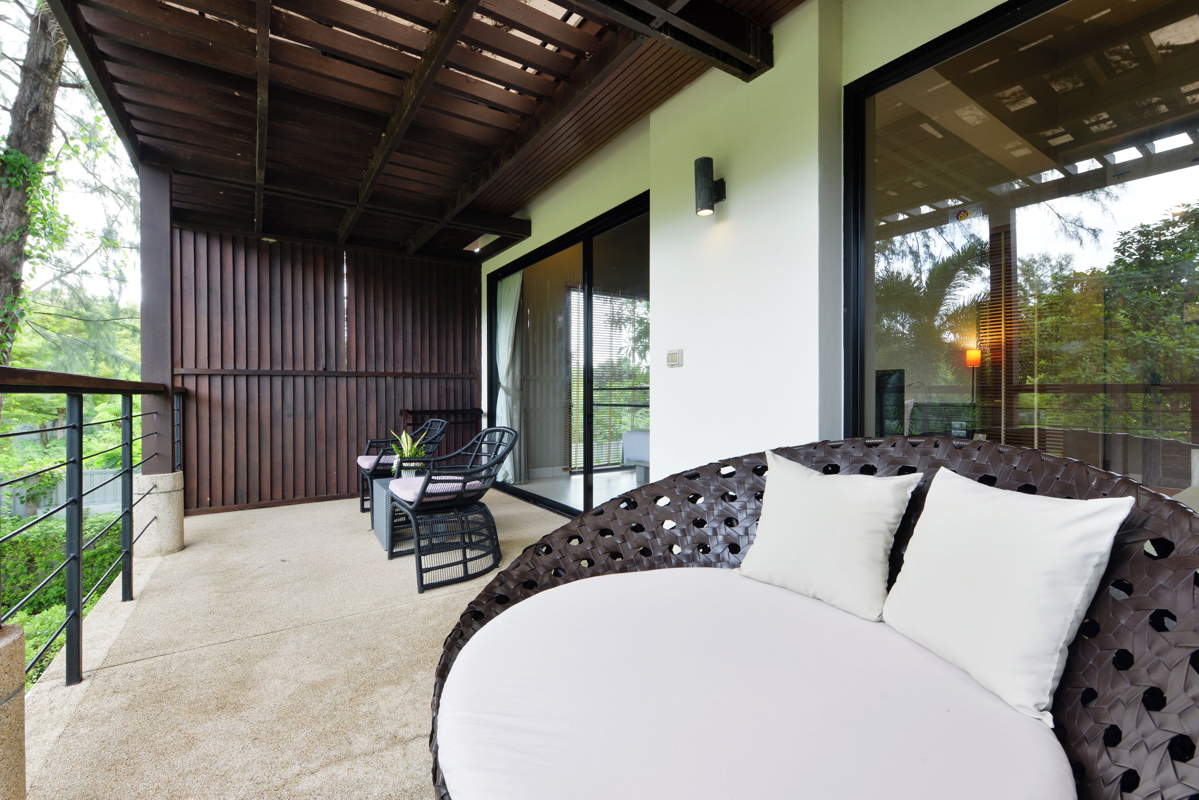A modern outdoor seating area with a round sofa and a dining table, surrounded by a wooden pergola and a glass railing overlooking a garden.