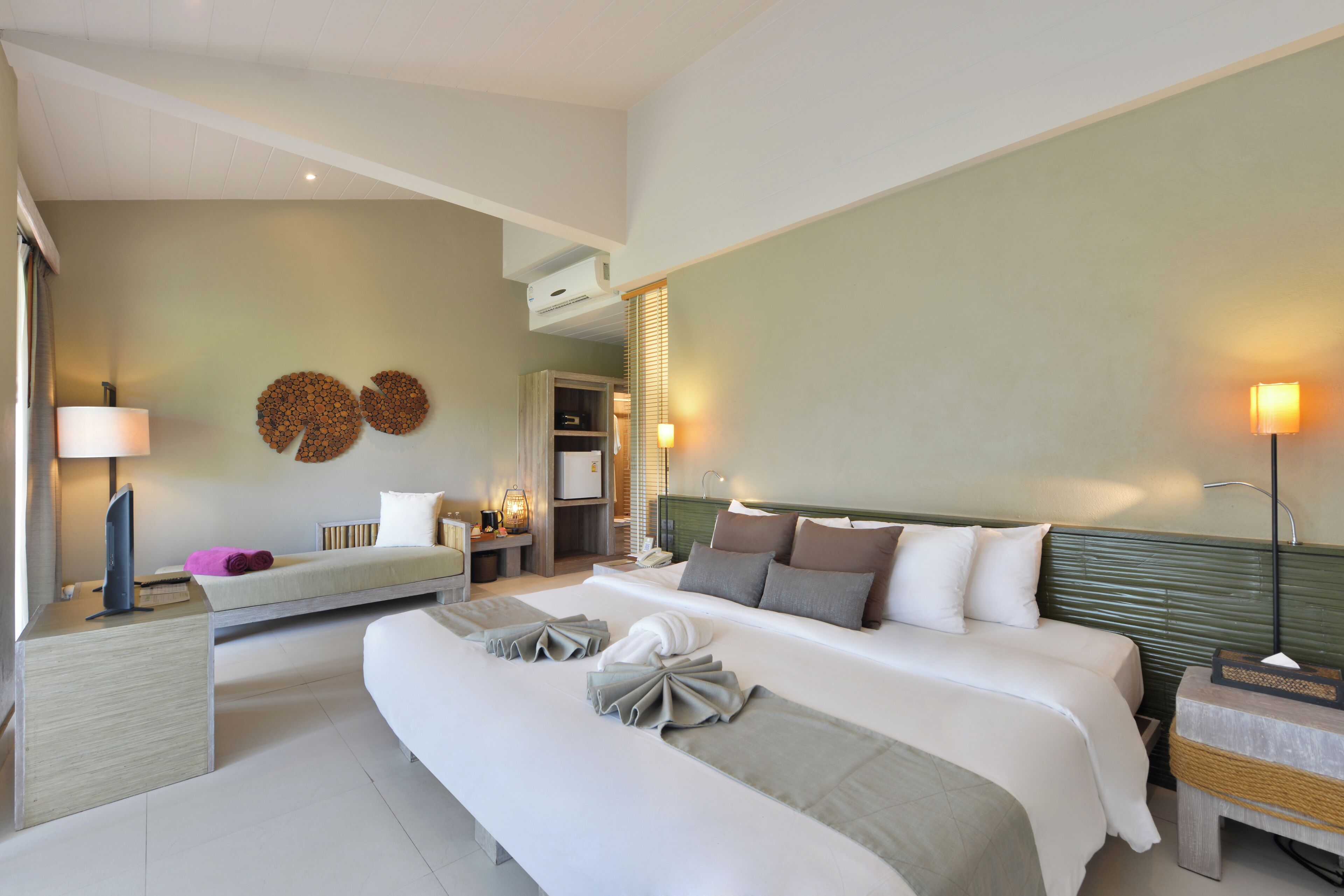 Une chambre d’hôtel moderne, dotée d’un grand lit, de tables de chevet, d’un bureau et d’une lampe.