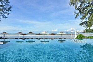 A clear blue infinity pool with lounge chairs and umbrellas, overlooking the ocean.