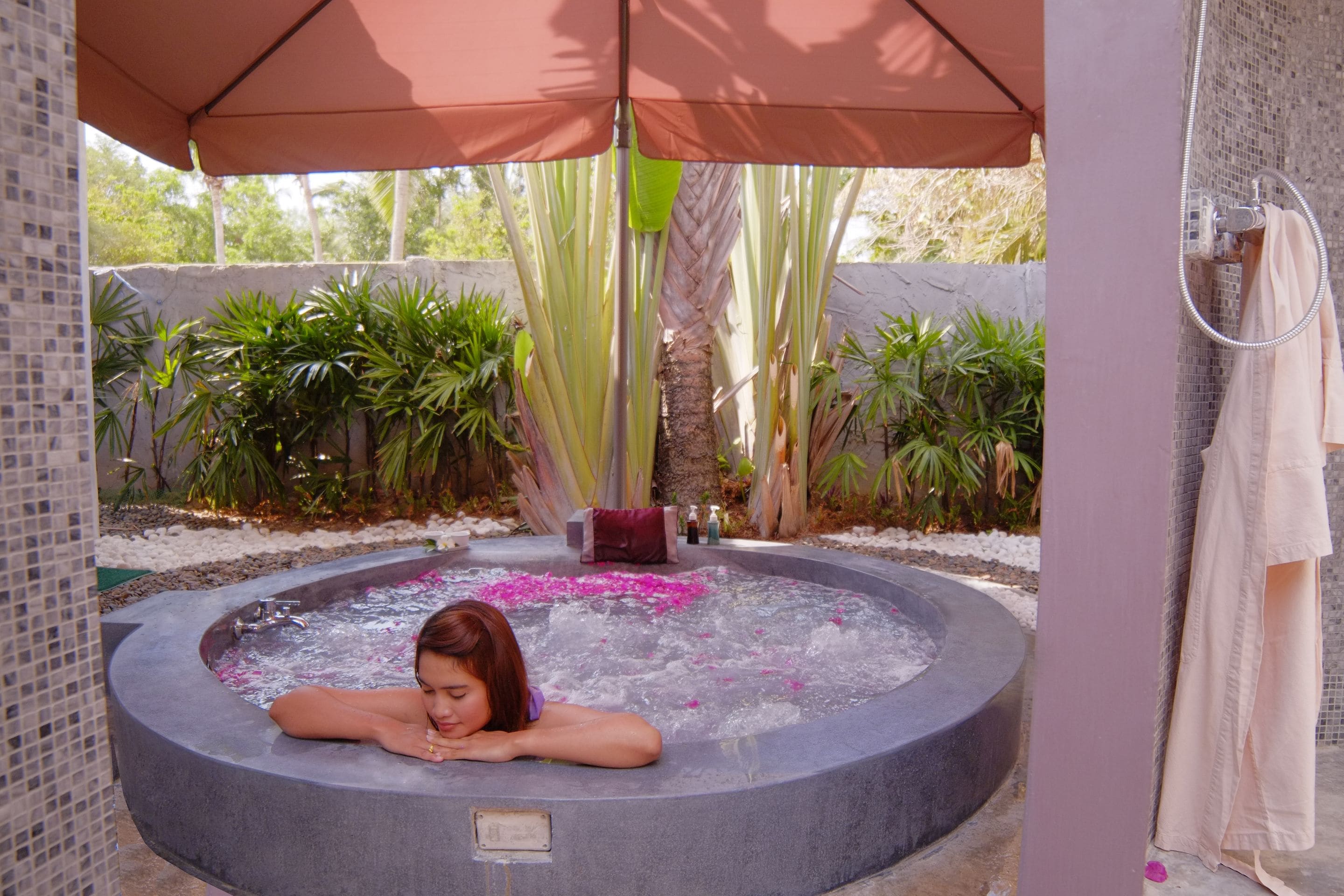 A spa area with a hot tub, surrounded by plants and a tiled wall.