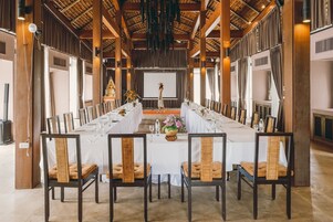 Una larga mesa de comedor con manteles blancos, rodeada de sillas de madera con respaldo trenzado.