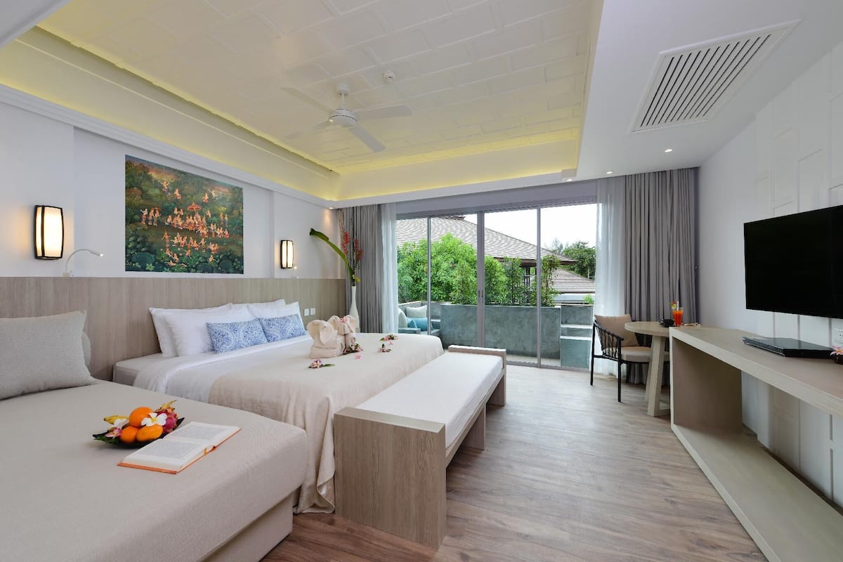 A hotel room with two beds, a desk, a TV, and a balcony with a view.