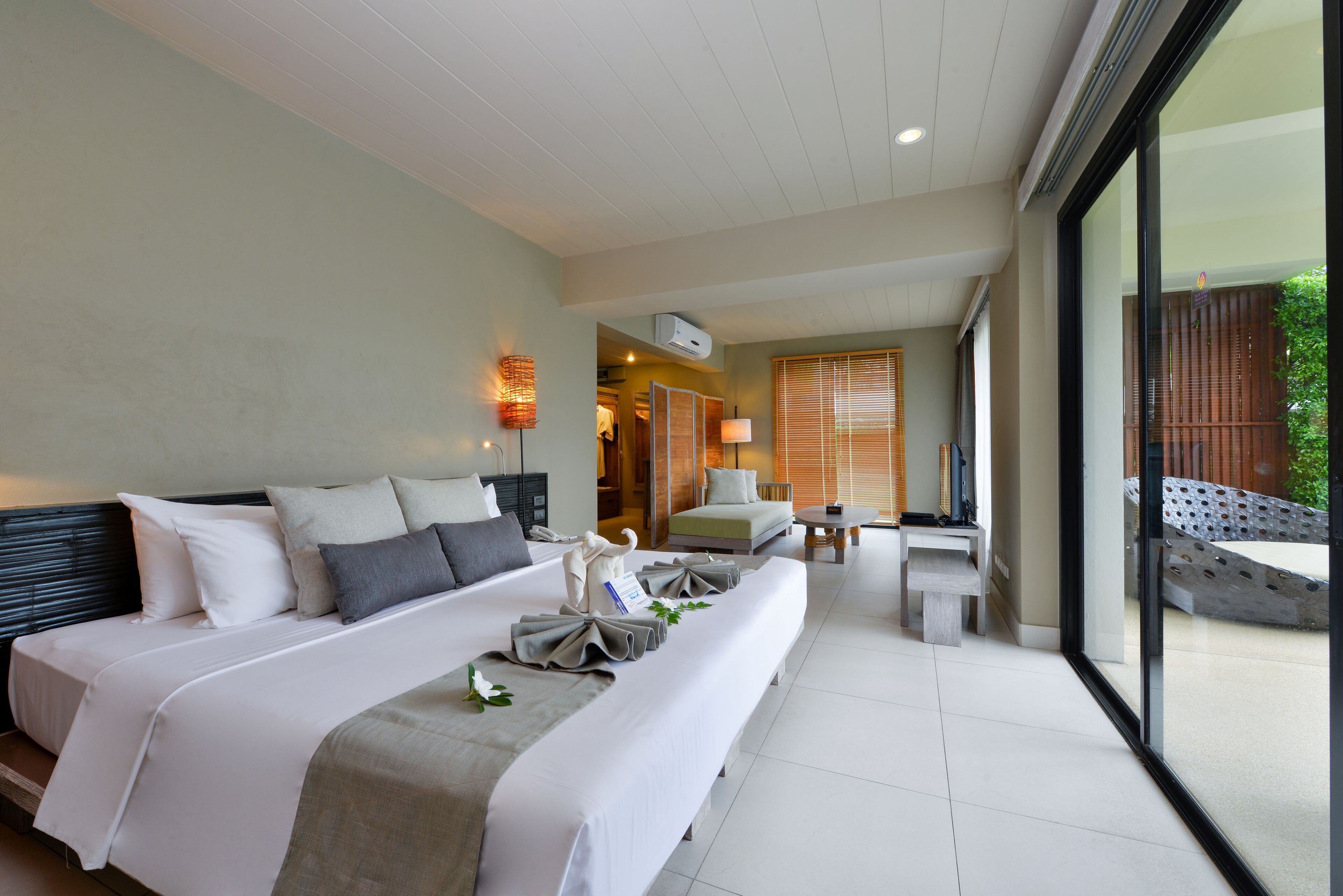 A hotel room with a large bed, a seating area with a table, and a view through a large window.