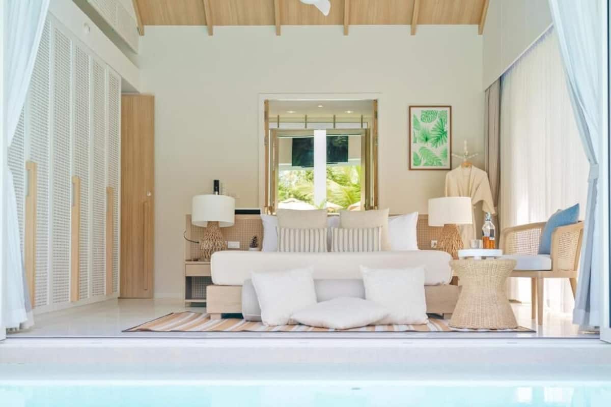 A modern bedroom with a large bed, bedside lamps, a view of greenery, and a window.