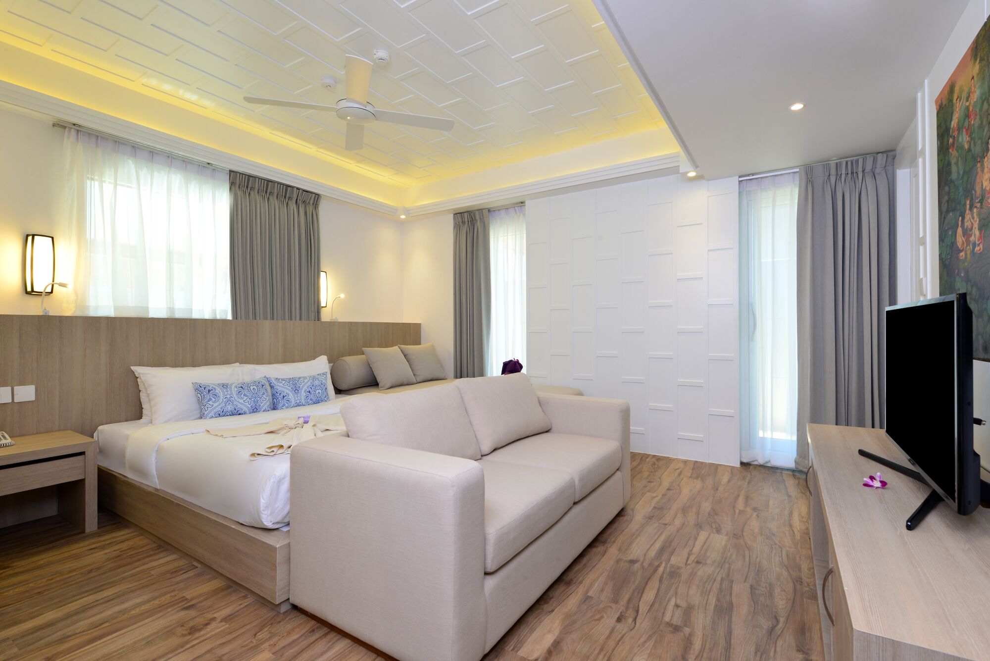 Une chambre d’hôtel moderne dotée d’un grand lit, d’un canapé, d’une télévision à écran plat et d’un ventilateur de plafond.